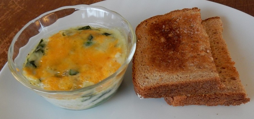 Eggs, cheese and spinach in ramekin with toast on plate 